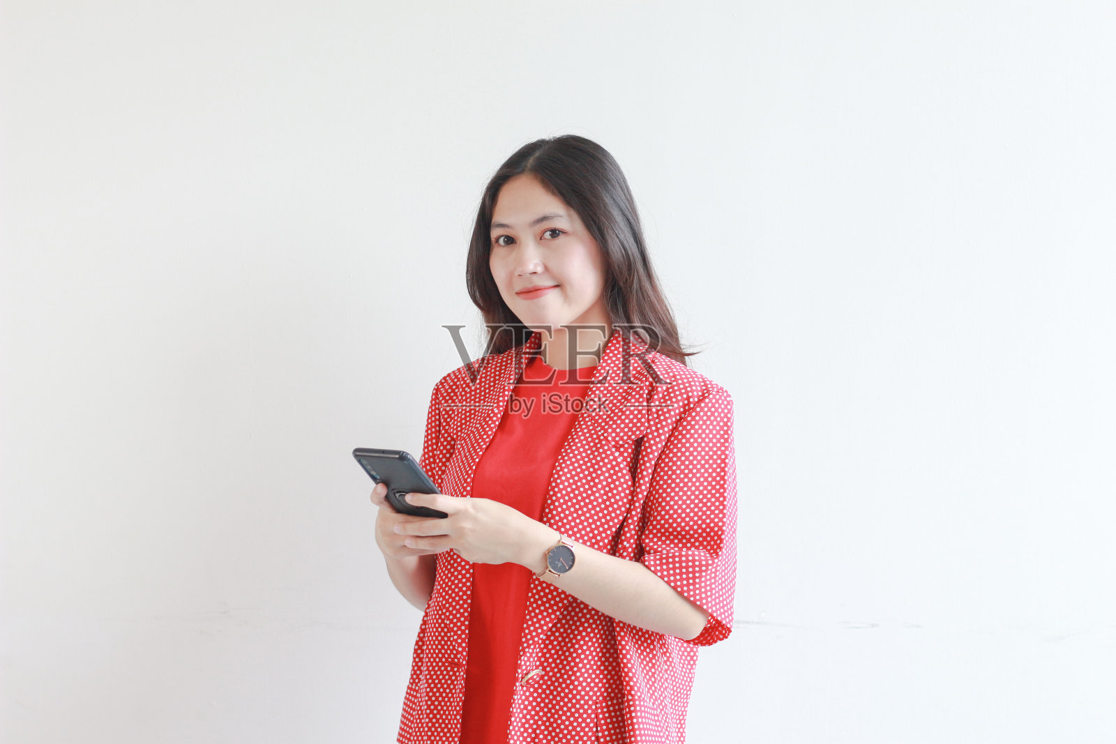 美丽的亚洲女人的肖像，穿着红色的衣服，拿着手机，脸上带着快乐的表情照片摄影图片