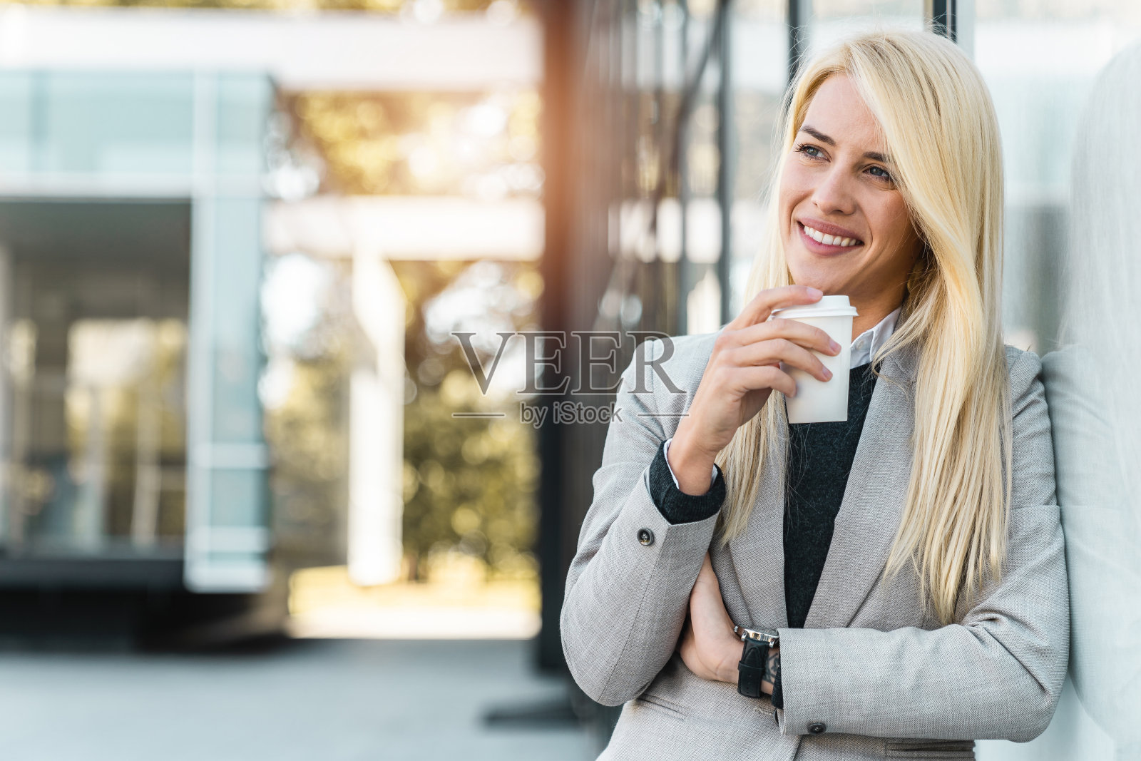 微笑自信的女商人手持咖啡杯在办公楼外沉思照片摄影图片
