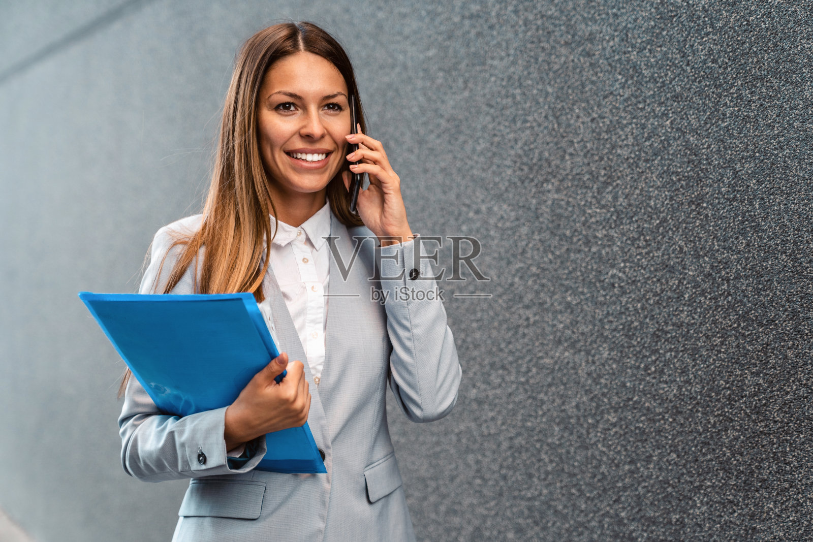 女房地产经纪人一边打电话一边拿着文件夹走在户外照片摄影图片