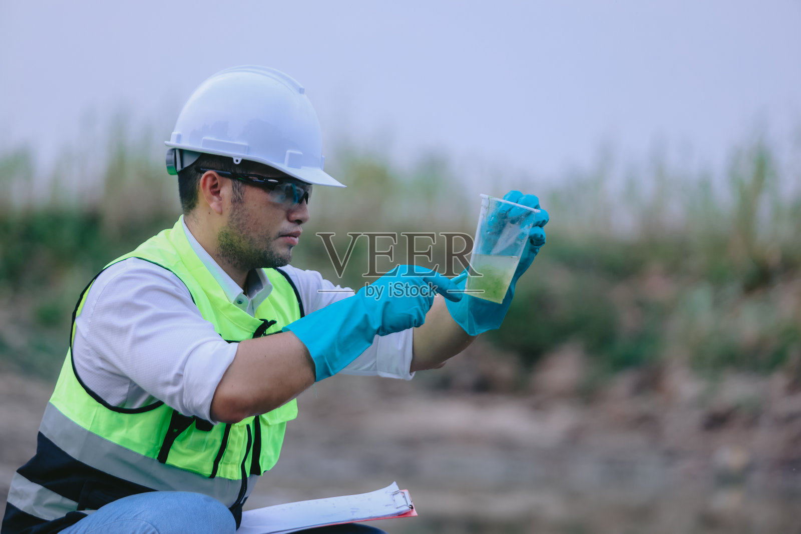 亚洲一名生态学家手持放大镜在湖中观察透明玻璃中的水。概念，探索，分析水质和生物从自然来源。生态学野外研究。照片摄影图片