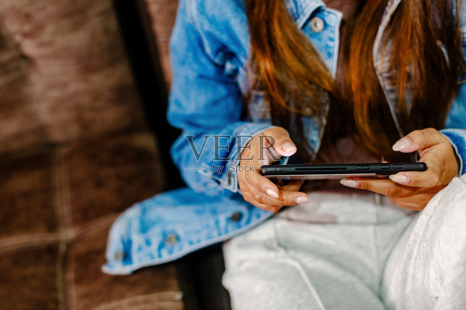 在棕色沙发上使用智能手机的女人的手特写。copyspace照片摄影图片