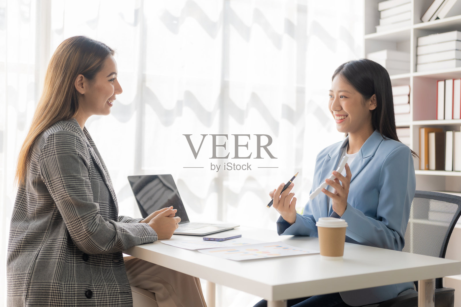 两个年轻的亚洲女商人在办公室用笔记本电脑做报告。同事们在新市场项目的文件分析中讨论财务数据。照片摄影图片