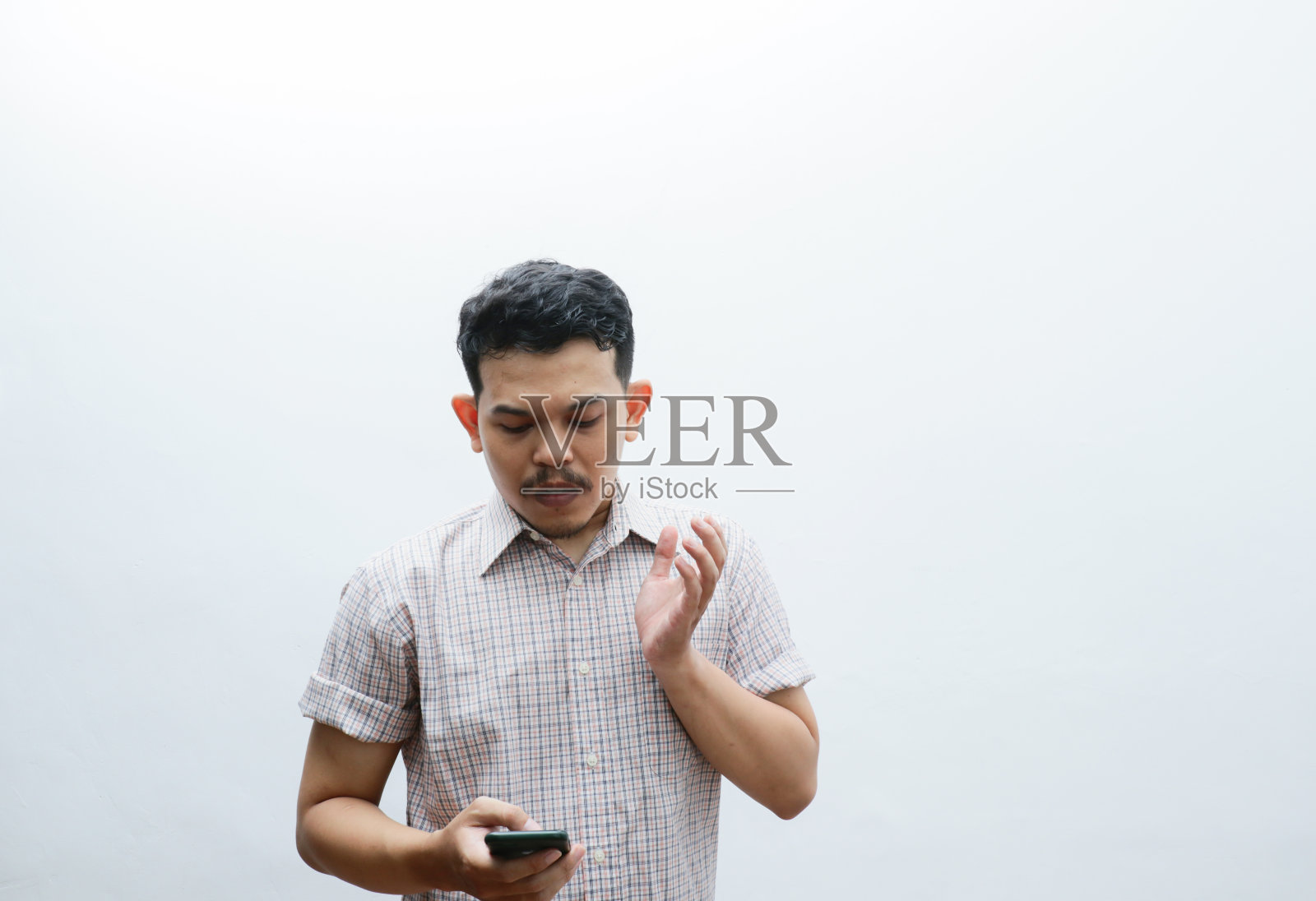 一名亚洲男子在看智能手机时露出困惑的表情照片摄影图片
