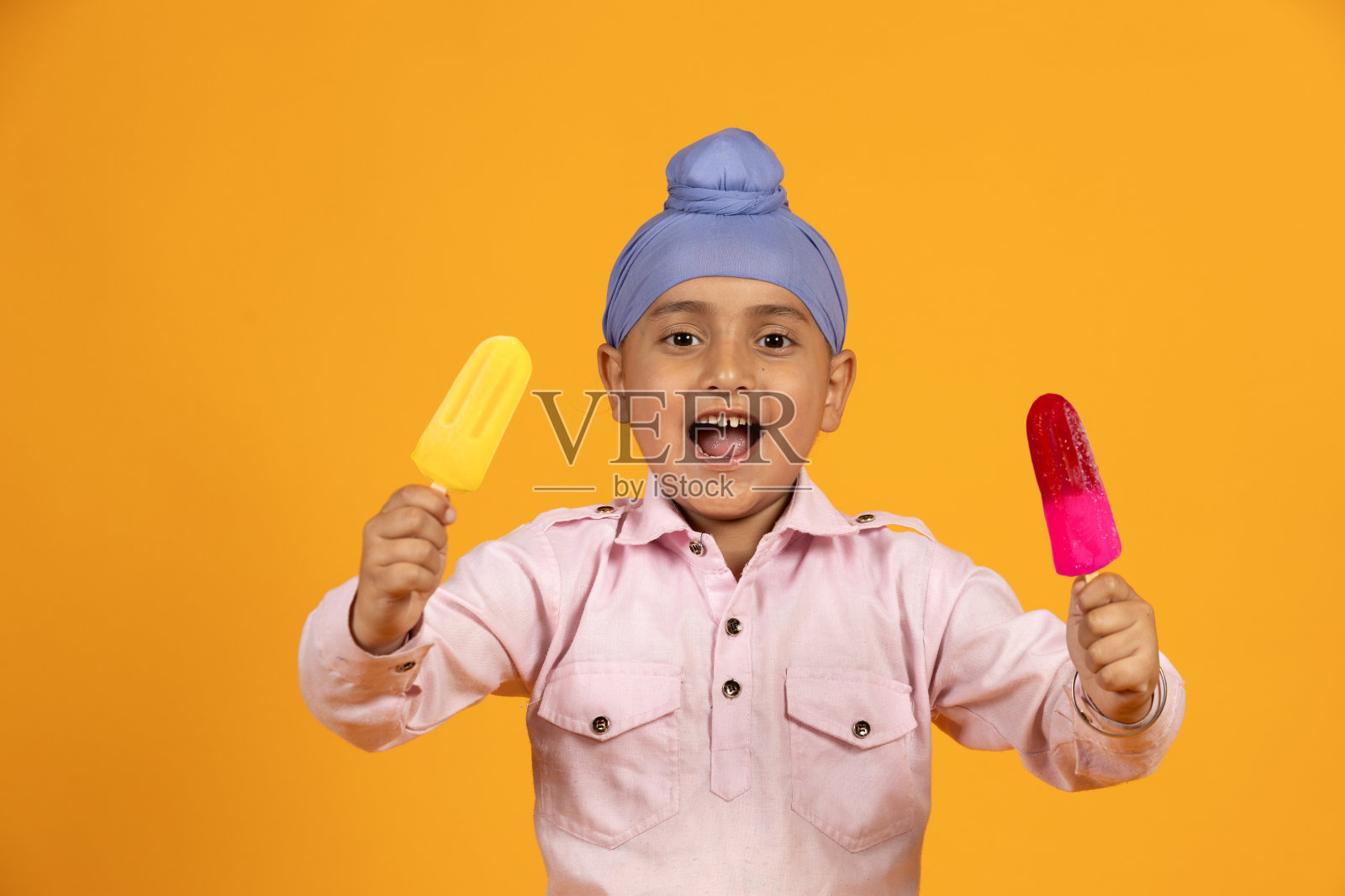快乐的锡克教印度孩子享受两种不同口味的冰淇淋或冰棍在夏天孤立的橙色背景。旁遮普的孩子吃着美味的糖甜点。不健康的饮食，享受食物。照片摄影图片
