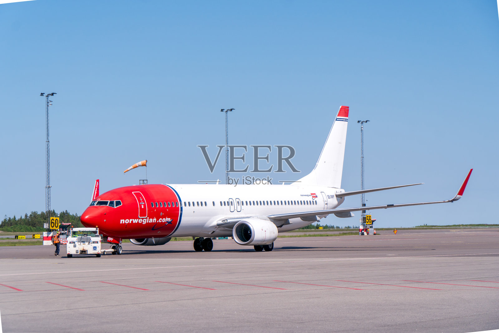 一架挪威航空公司的波音737-800，典型的红白相间的涂装，停在哥德堡兰德维特机场，旁边是一辆推力车。明亮的太阳照片摄影图片