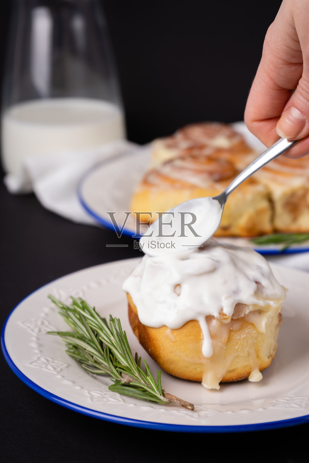 白色盘子上的肉桂卷，蓝边装饰着迷迭香和一罐牛奶照片摄影图片