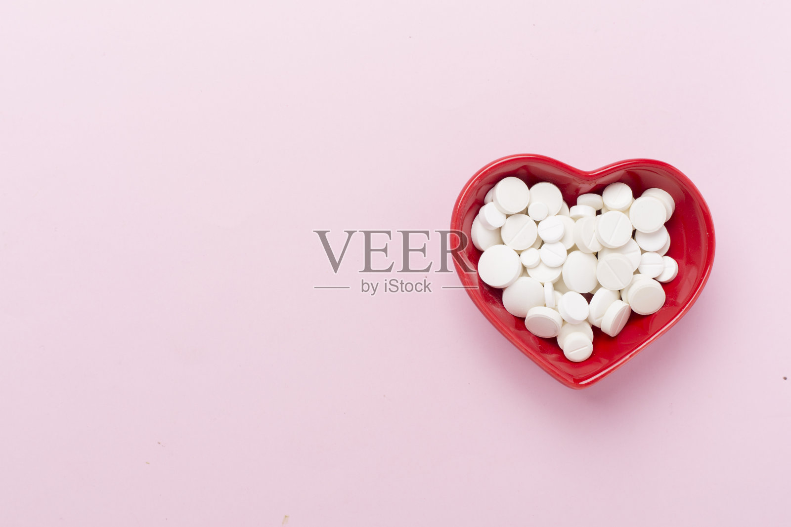 彩色背景上的心形碗中的药物，俯视图照片摄影图片