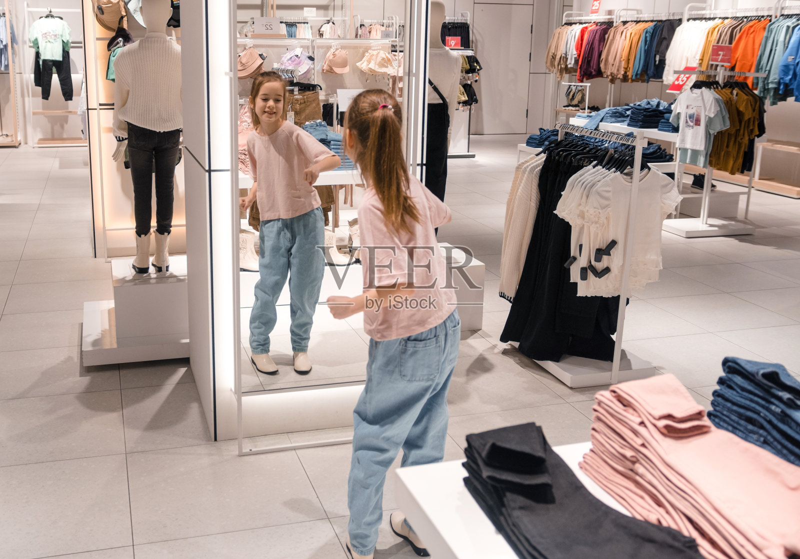 晚上，小女孩在灯火通明的服装店里试穿衣服照片摄影图片