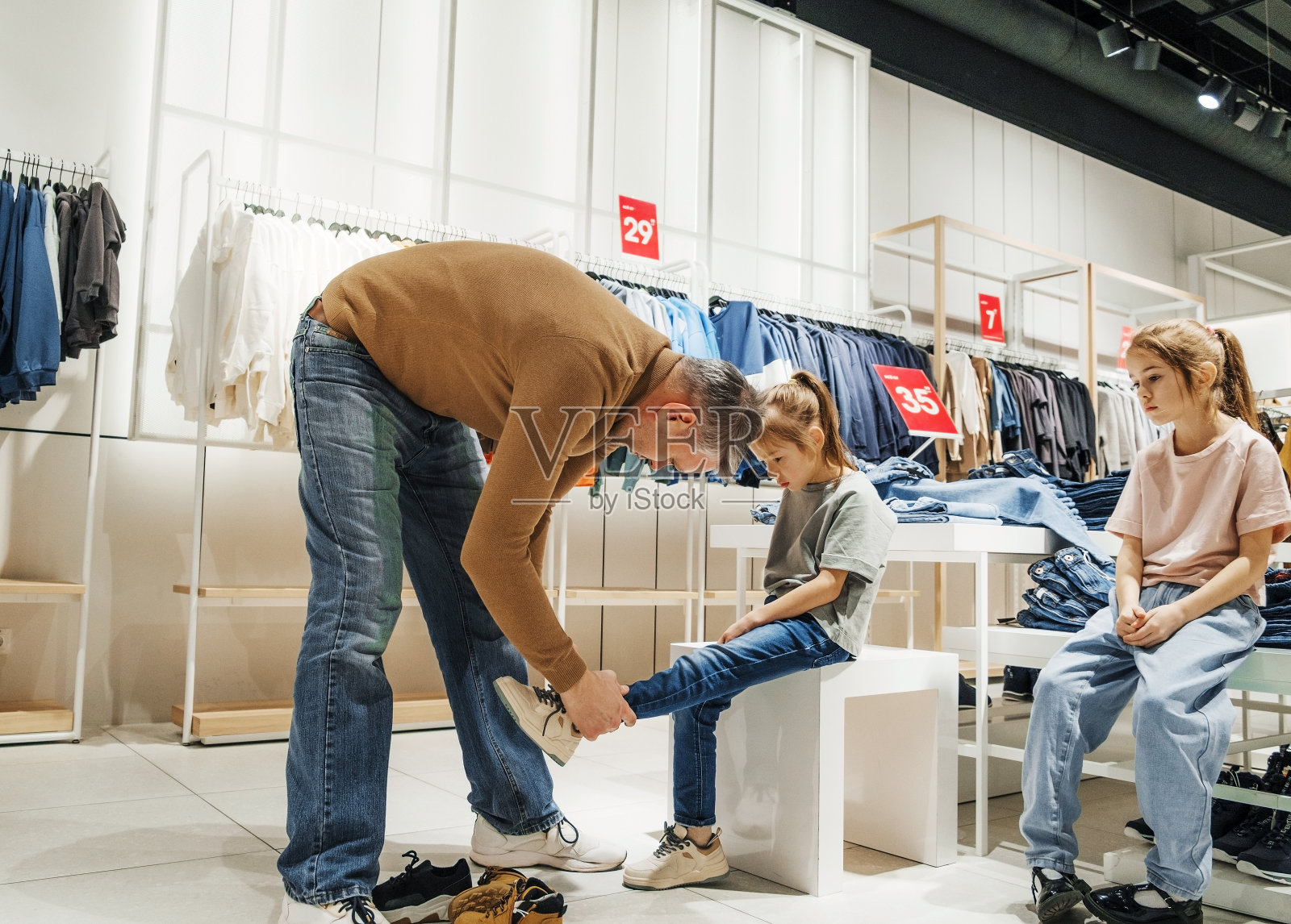 白天，父亲在现代服装店帮女儿试鞋照片摄影图片