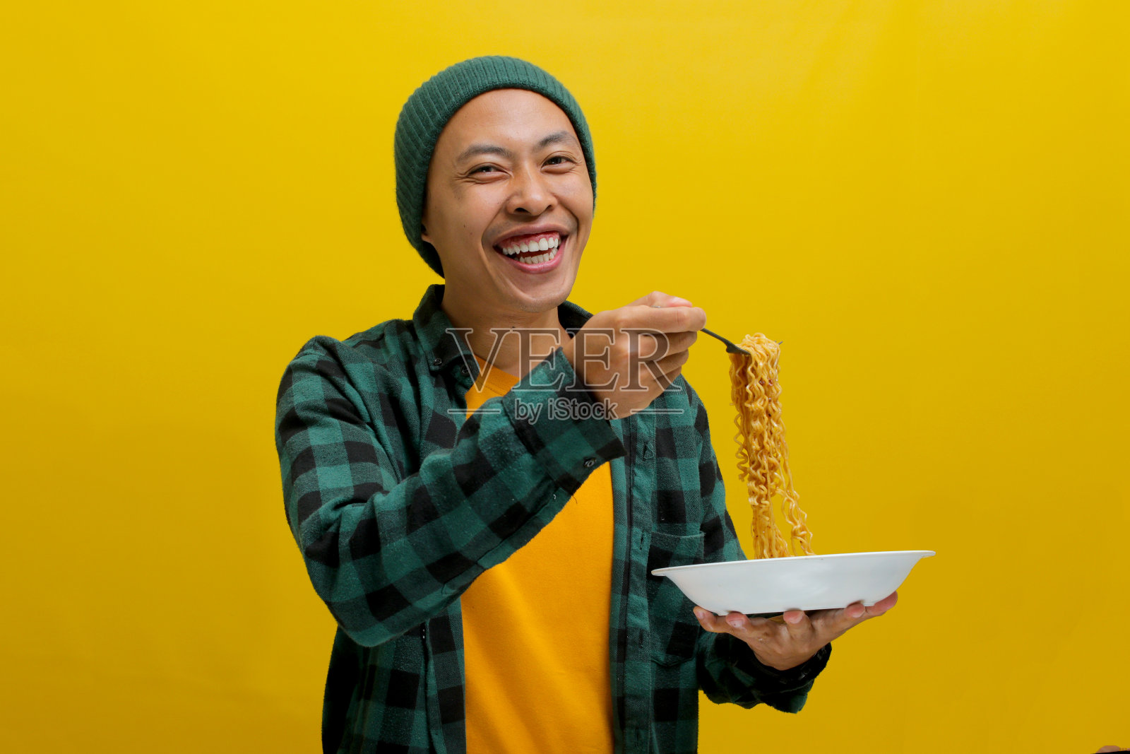 一个亚洲男人用叉子品尝着方便面，背景是鲜艳的黄色照片摄影图片