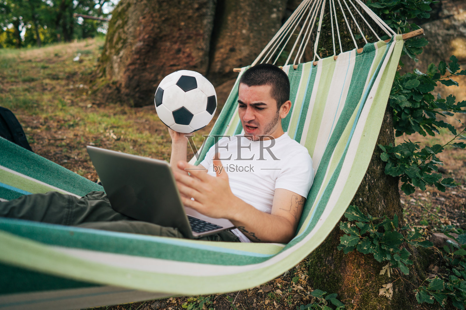 一个年轻人，手里拿着一个足球，在笔记本电脑上疯狂地观看足球比赛照片摄影图片