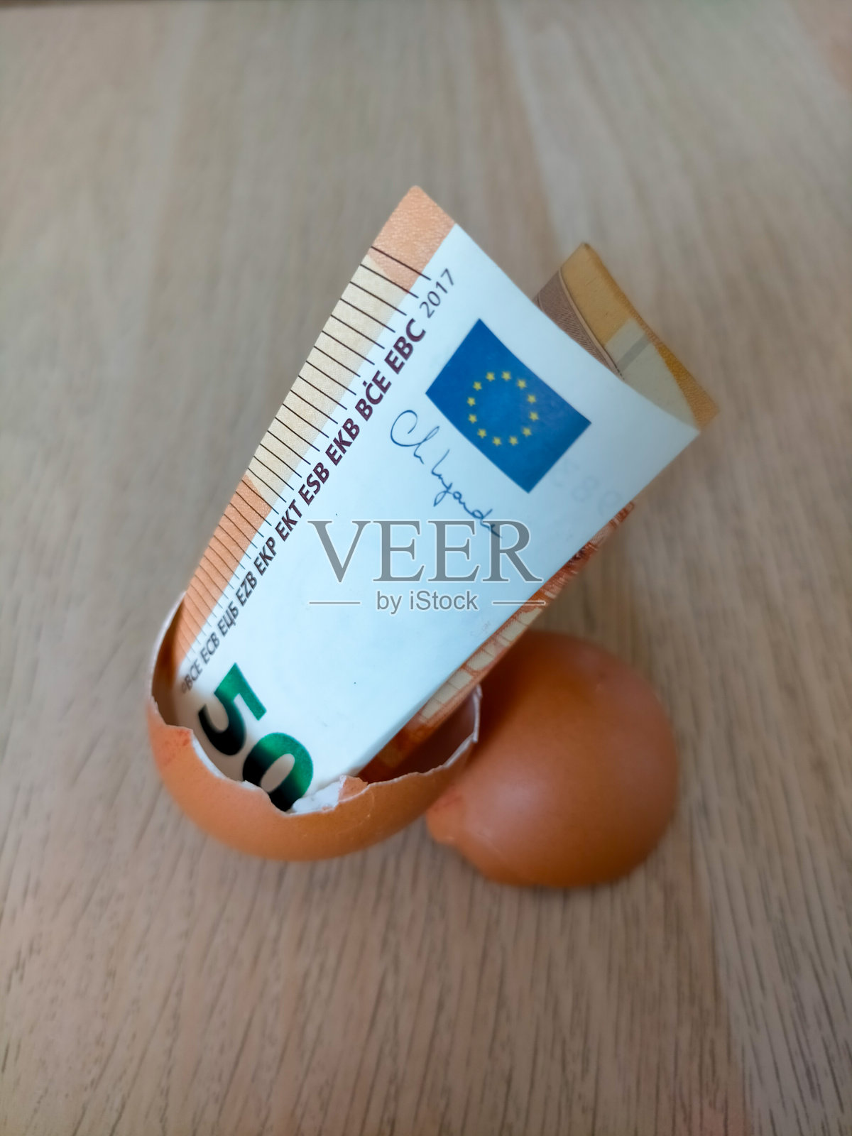 在浅棕色的木制背景上，一张50欧元的纸币在一个破碎的鸡蛋里照片摄影图片