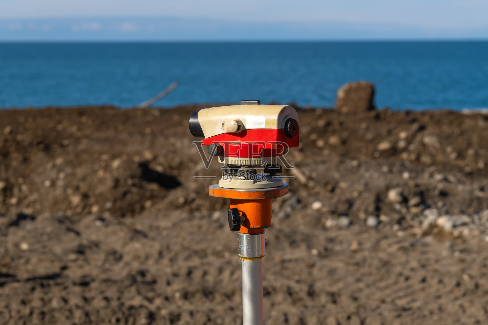 用于测量建筑工地角度和距离的光学水准仪或测量仪器的近景图像。在后台，建筑工人使用起重机和推土机来搬运材料。海照片摄影图片