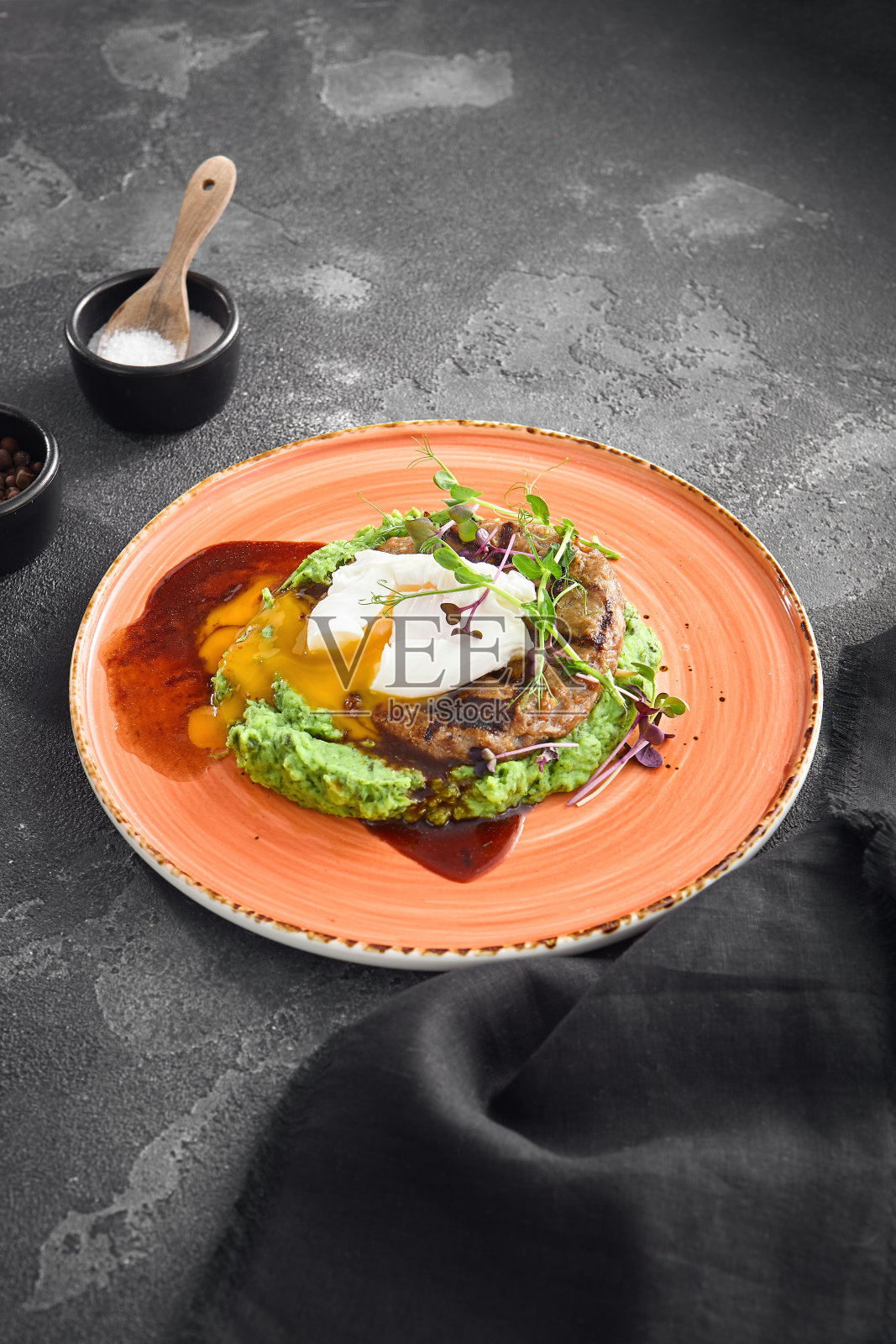 多汁的牛排铺在绿色豌豆泥上，配上一个完美的荷包蛋，放在黑色背景下的陶瓷盘子里照片摄影图片