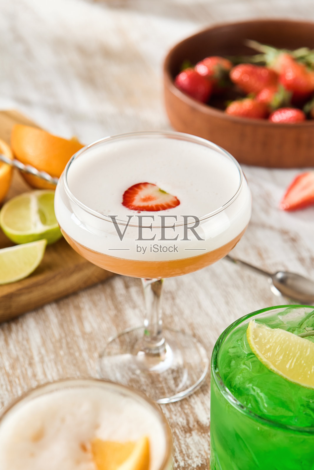 清爽的草莓酸鸡尾酒在优雅的玻璃器皿在现代酒吧，伴随着新鲜的酸橙和橘子在木桌照片摄影图片
