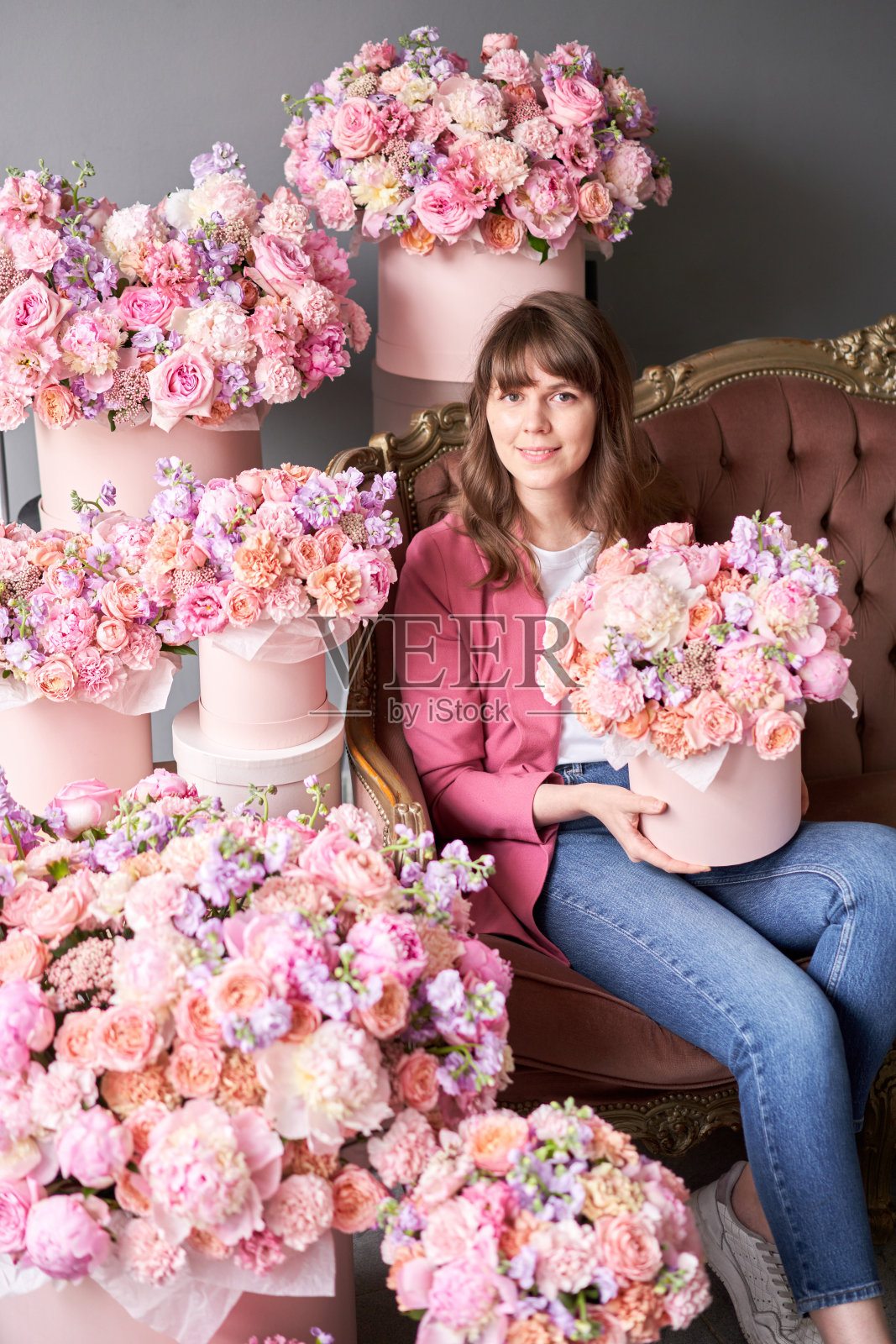 一个快乐的年轻女孩手里拿着一盒花，闻着花的香味。一个美丽的女人坐在沙发上，周围都是鲜花。照片摄影图片