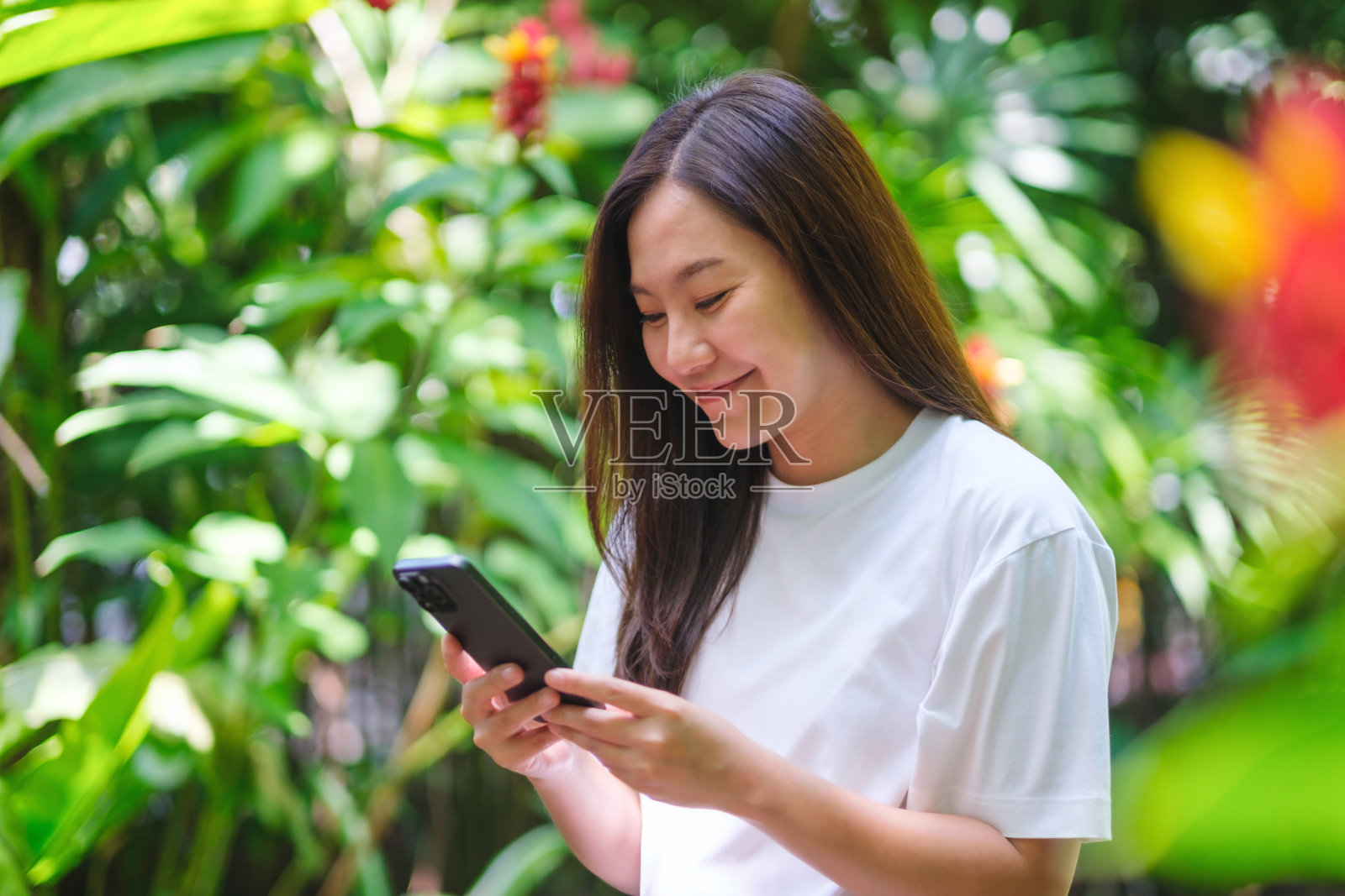 一名年轻女子在花园里手持并使用手机的肖像照片摄影图片