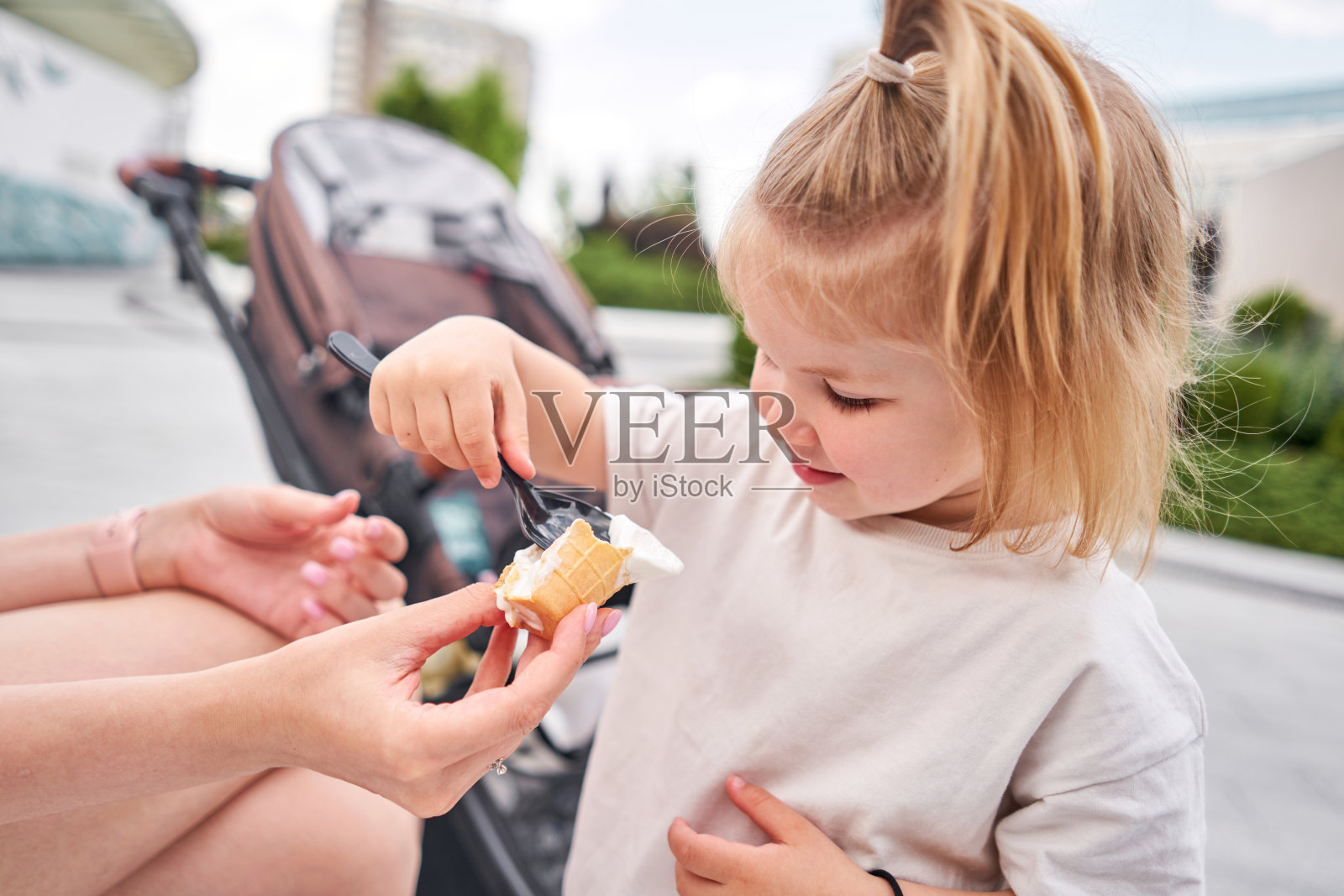 饥饿的孩子喜欢在户外吃冰淇淋。一个可爱的婴儿在城市公园散步时舔着奶油冰淇淋的肖像，户外活动。照片摄影图片