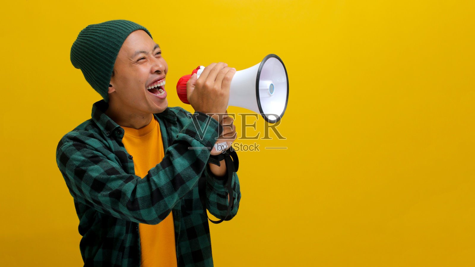 兴奋的亚洲男子与扩音器宣布特别优惠或销售在黄色背景照片摄影图片