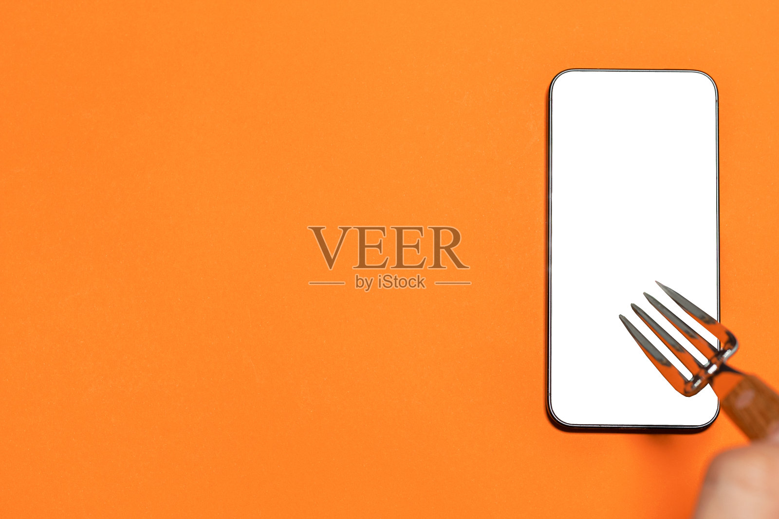 拿着叉子的手拿着黑屏手机。橙色背景。网上食品购物。带有复制空间的图像。照片摄影图片