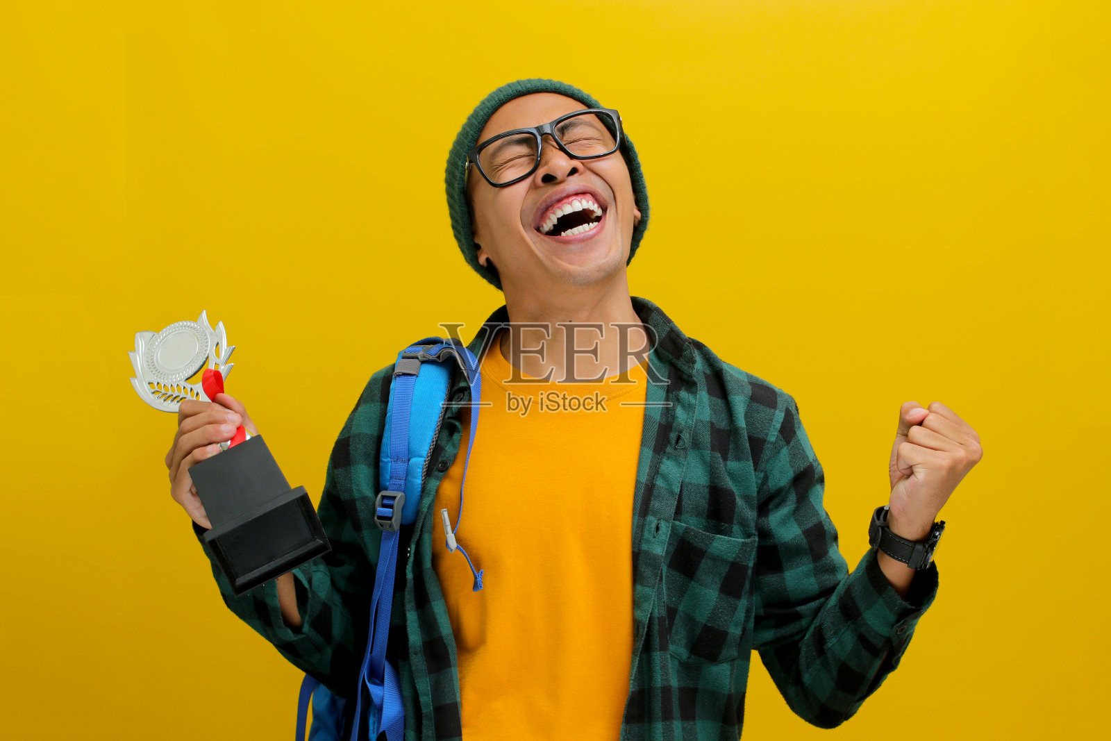 一个聪明的亚洲男学生举起拳头，做出“是”的手势，庆祝赢得奖杯照片摄影图片