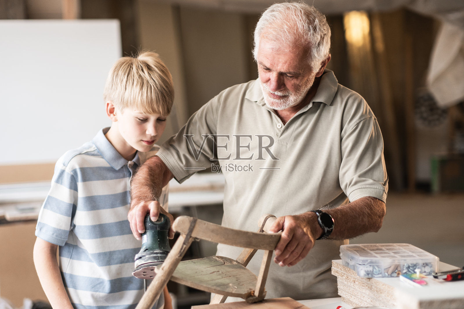 一位祖父在他的木匠作坊里教他的孙子如何修理家具。照片摄影图片