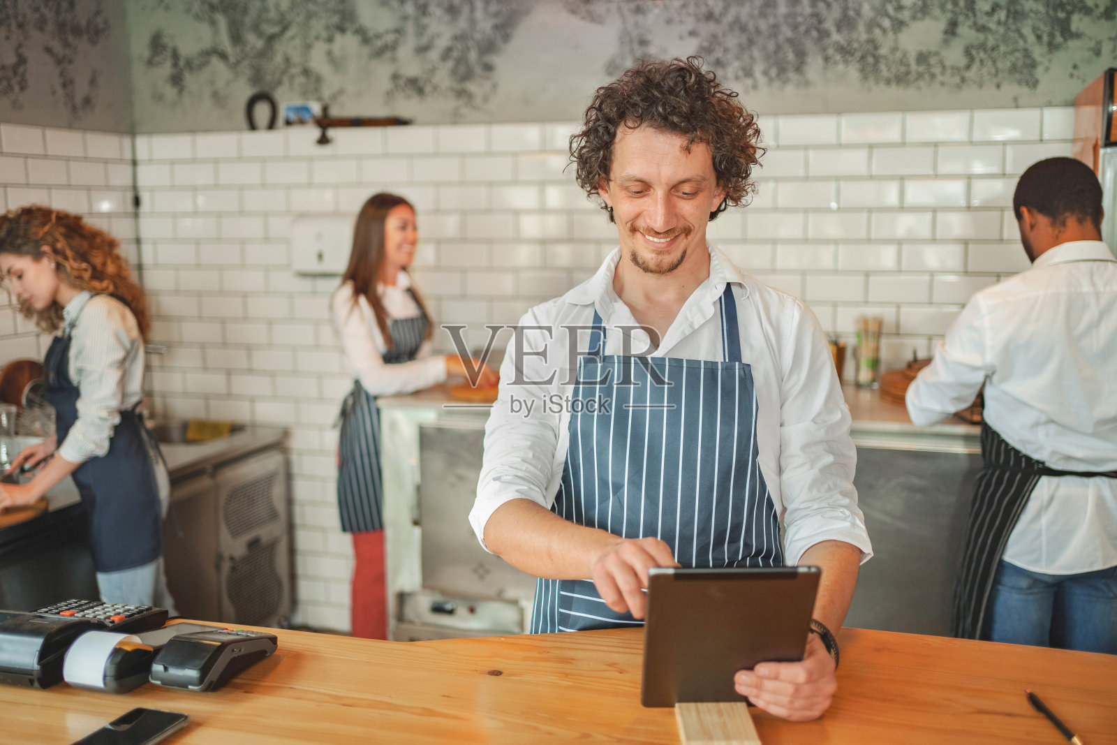 穿着围裙的白人男性员工在吧台后面摆弄电子平板电脑照片摄影图片