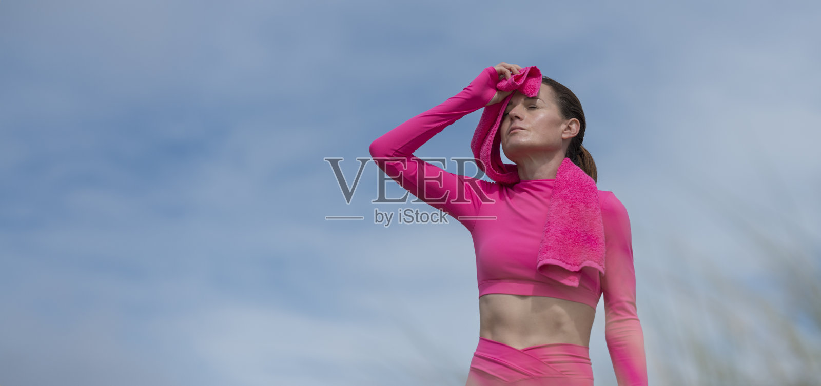 运动的跑步者用毛巾擦头，粉红色的运动服，蓝色的天空背景照片摄影图片