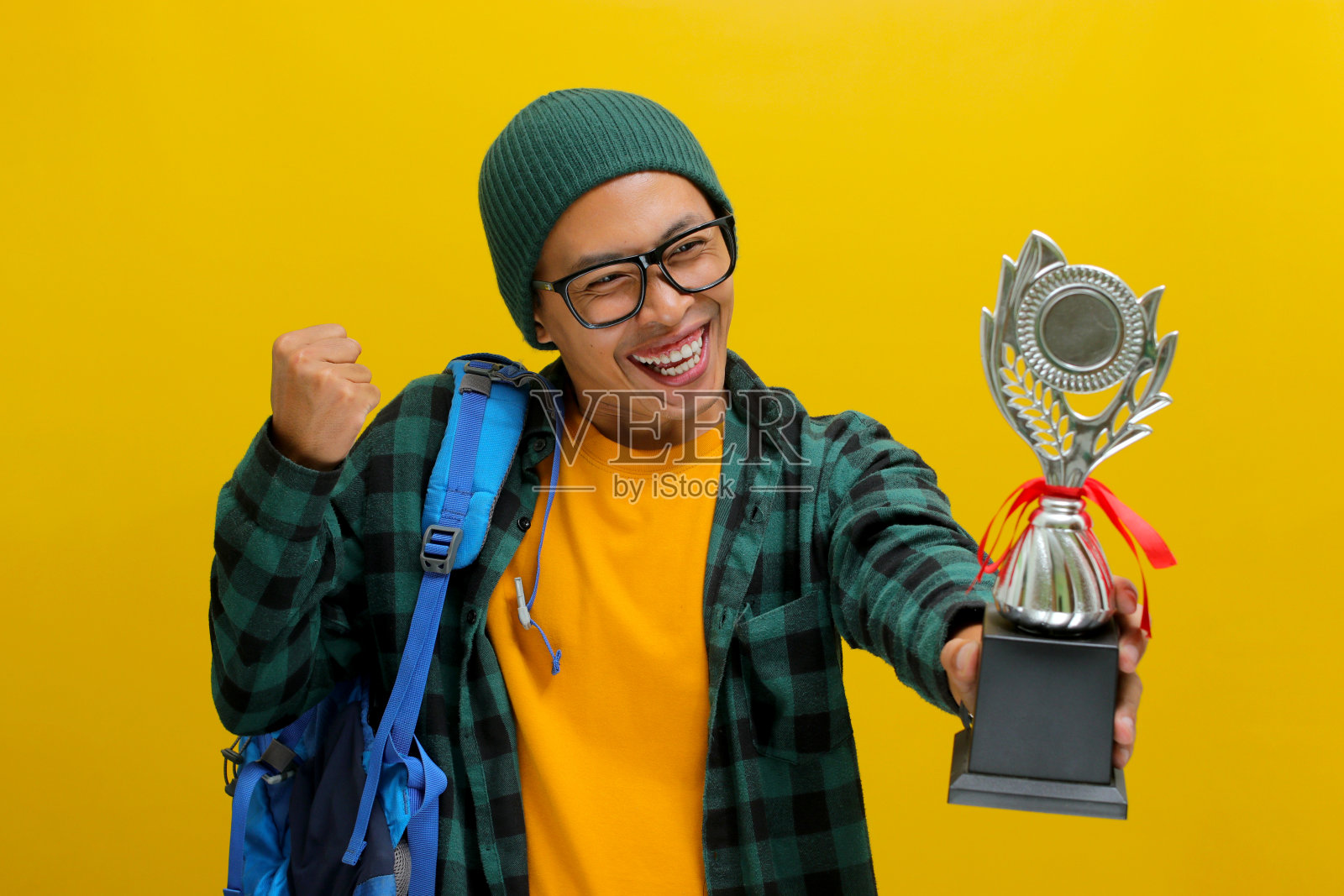 一个聪明的亚洲男学生举起拳头，做出“是”的手势，庆祝赢得奖杯照片摄影图片