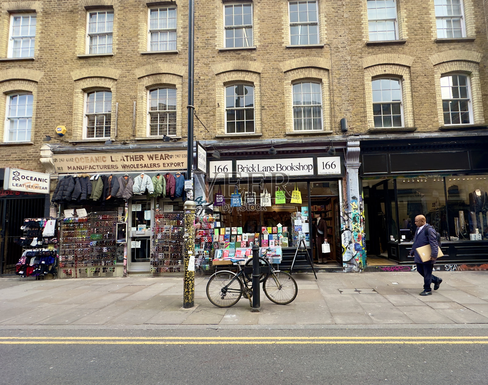 海洋皮具店和砖巷书店的景色，偶然有行人走在人行道上，一辆自行车靠在柱子上，英国伦敦。照片摄影图片