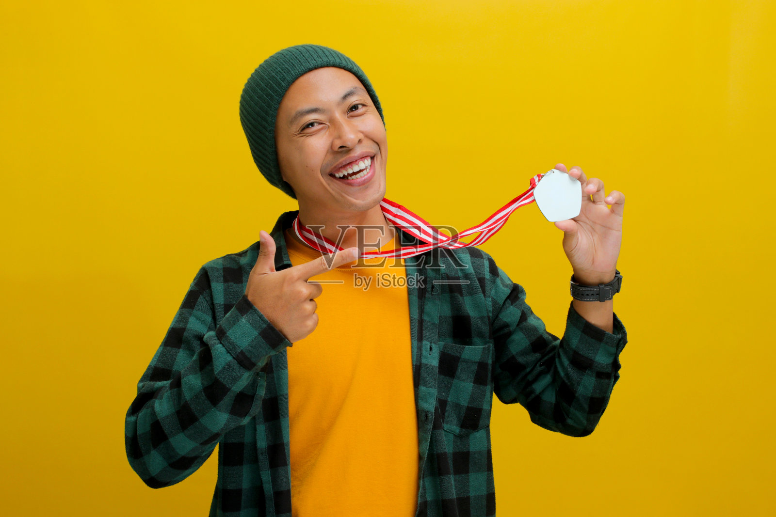 一个骄傲的年轻亚洲男子站在黄色的背景下指着自己的奖牌微笑照片摄影图片