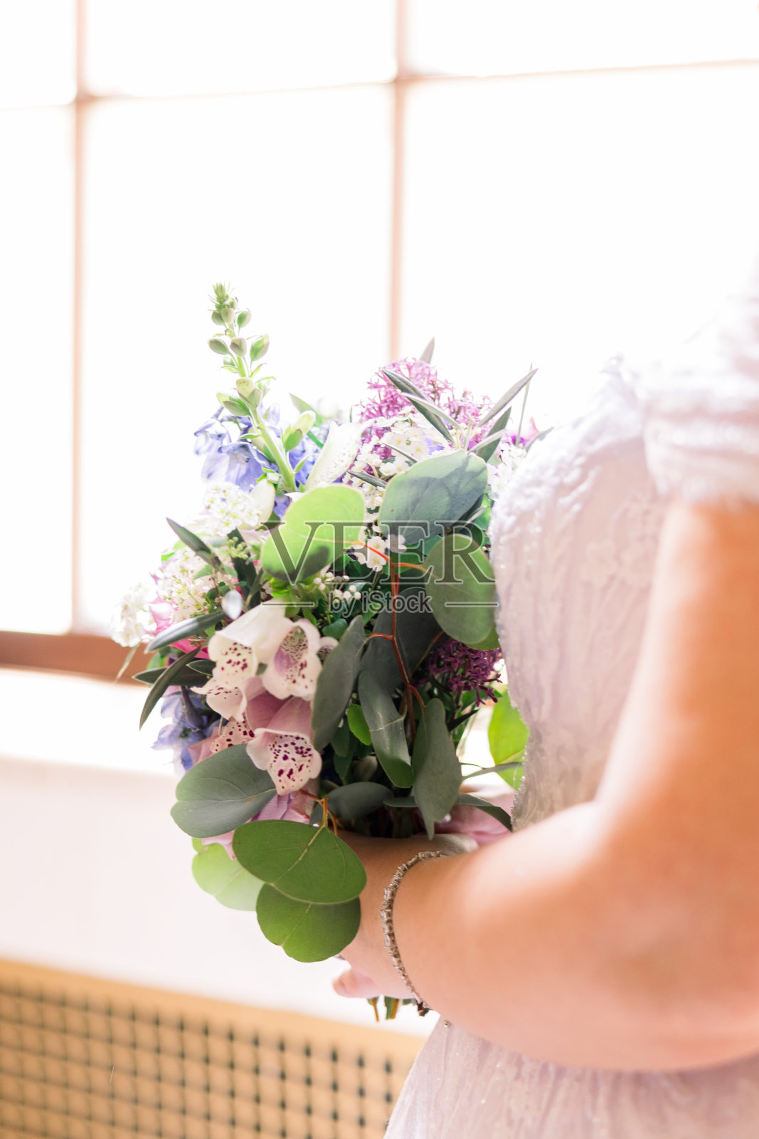 身着白色婚纱的新娘手持一束鲜花的特写。照片摄影图片