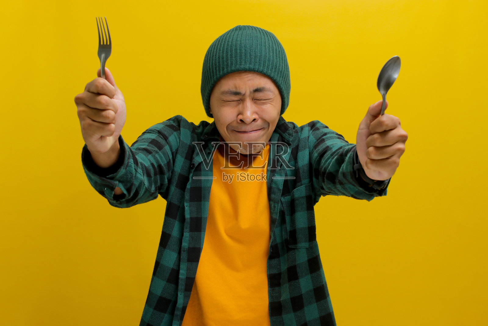 饥饿的年轻亚洲人想象美味的食物，拿着勺子和叉子照片摄影图片