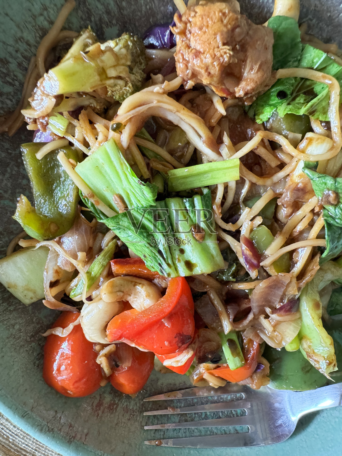 全帧图像碗炒熟的食材，堆切碎的混合蔬菜和面条，红色和绿色的甜椒，西兰花，洋葱，红白菜，羽衣甘蓝，金属叉子，高架视图，健康的饮食理念照片摄影图片