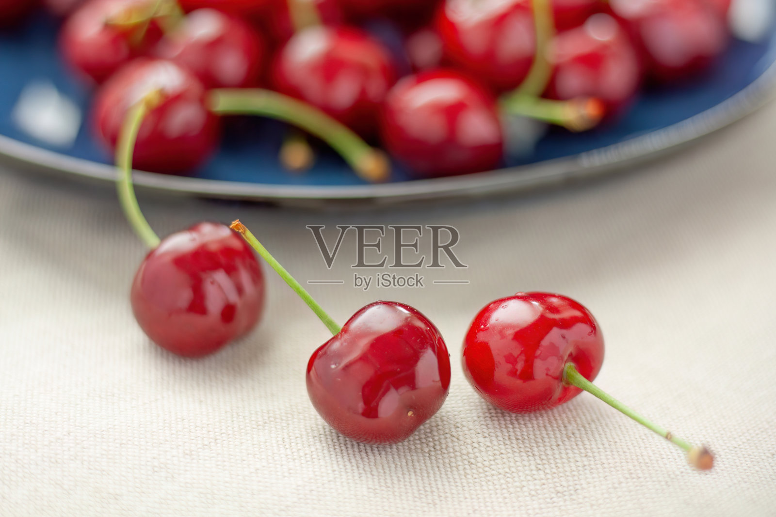 纺织品上蓝色盘子上的樱桃特写。照片摄影图片