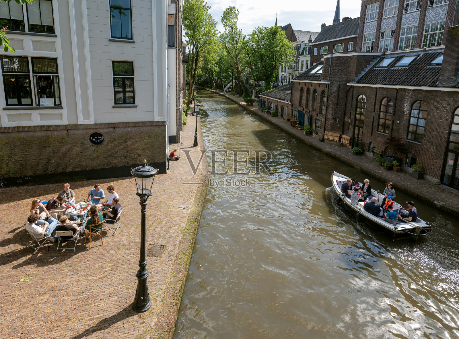 年轻人在乌得勒支的老河堤上享受美好的天气,而船只经过照片摄影图片