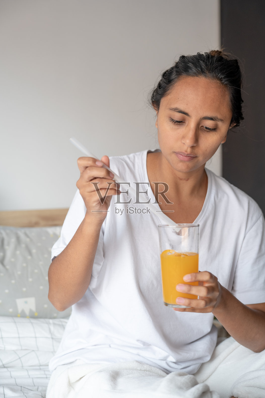 年轻女子白天在她的房间里穿着睡衣躺在床上用闪光灯喝橙汁照片摄影图片