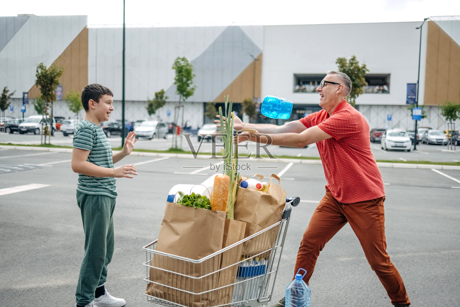父子俩买完东西拎着纸袋走向汽车，玩得很开心照片摄影图片