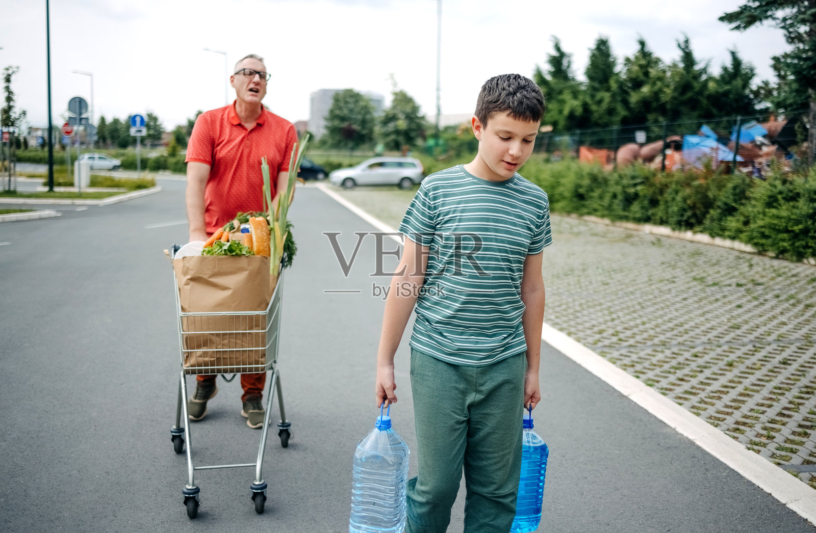 父子俩买完东西拎着纸袋走向汽车，玩得很开心照片摄影图片