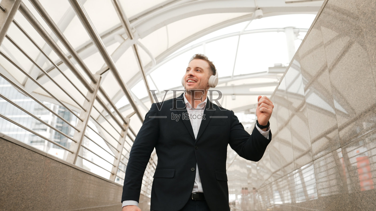 在现代的走廊里，熟练的商人随着耳机里的音乐跳舞。彬彬有礼的。照片摄影图片