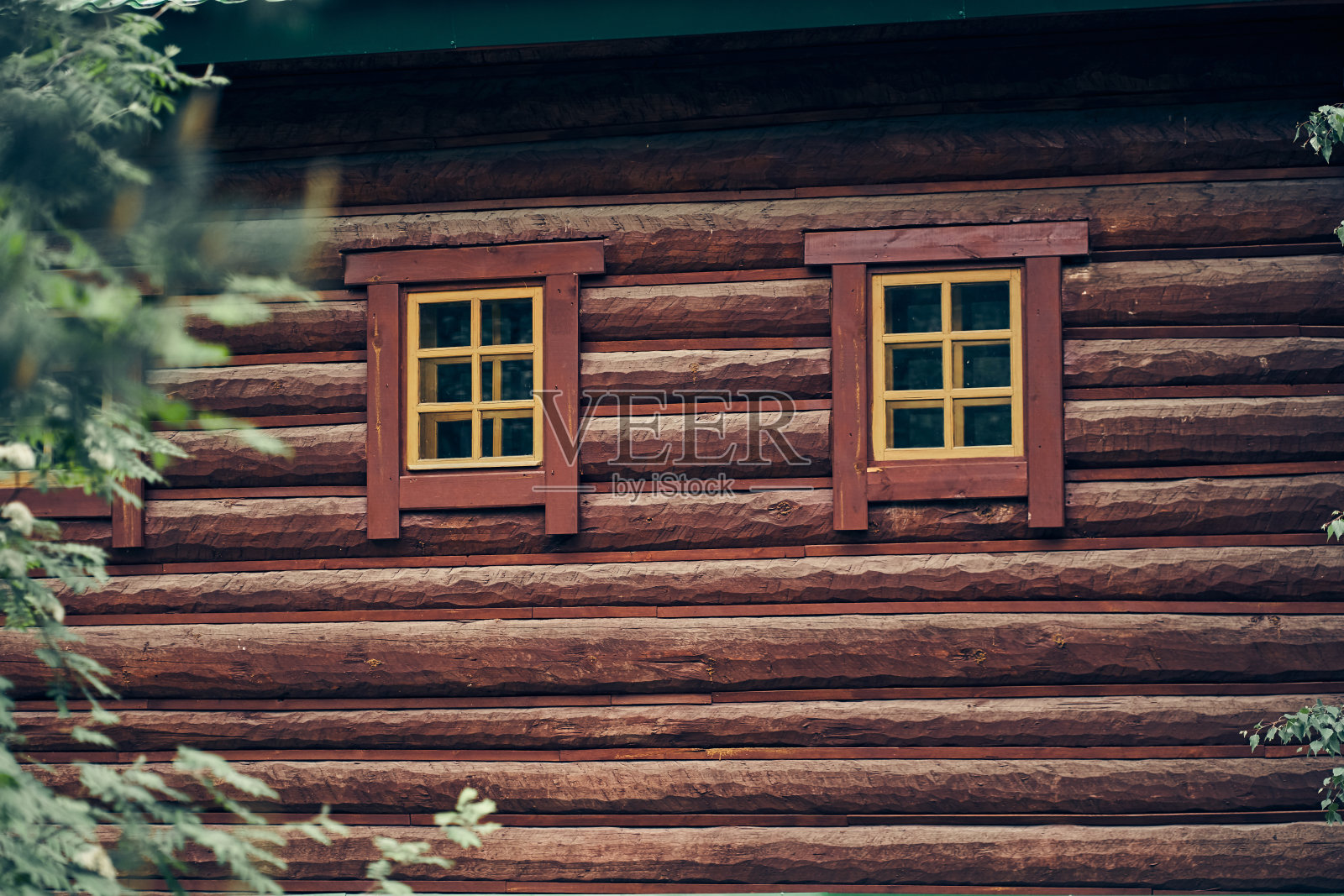 建筑的立面由圆形原木和棕色深色窗框组成。建筑结构与设计。房子里的窗户。照片摄影图片