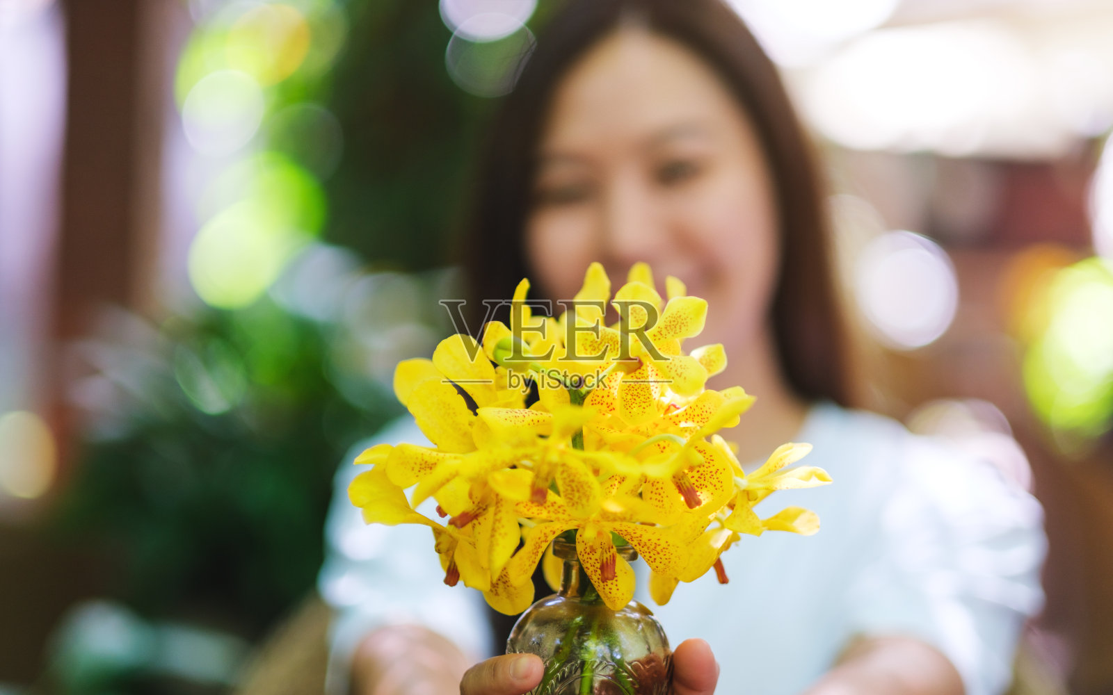 模糊的图像，一个女人拿着并送了一个黄色兰花的花瓶照片摄影图片