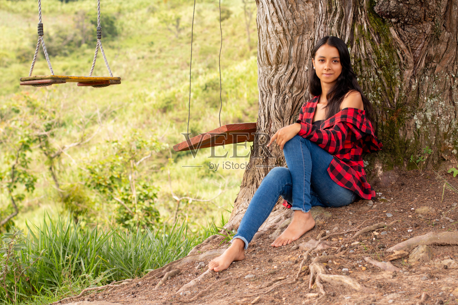 生活方式:一名拉丁裔女子赤脚坐在公园的一棵大树下放松照片摄影图片