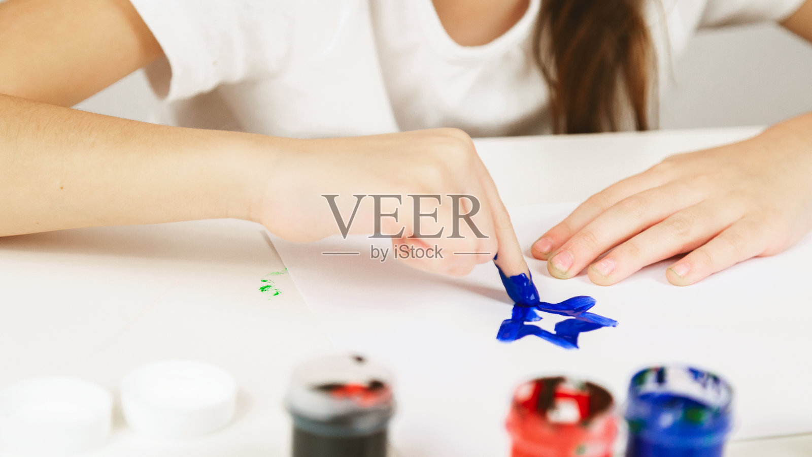 一个小女孩在室内的桌子旁用手指画画。儿童创造力的概念。照片摄影图片