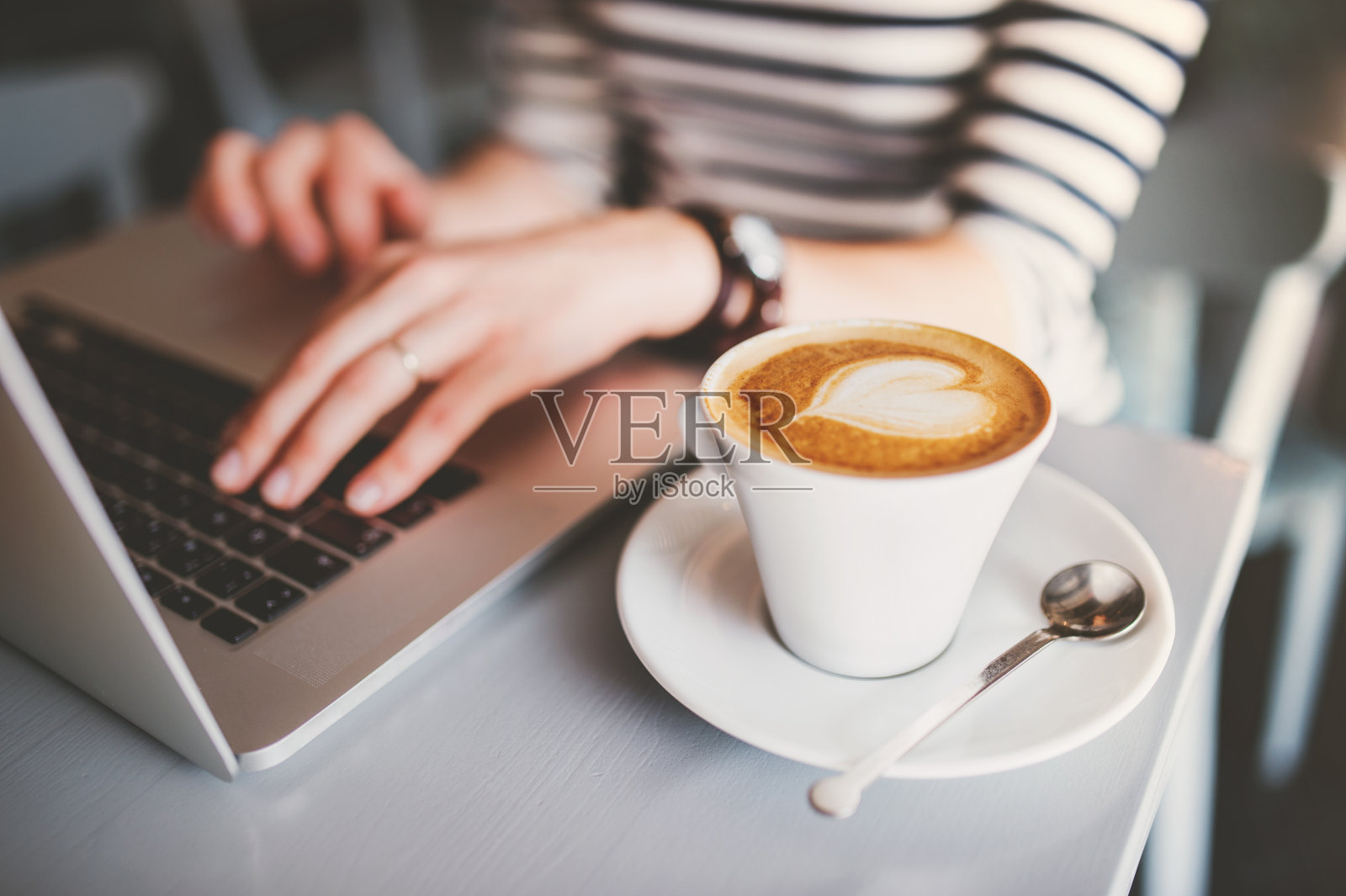 在咖啡店远程工作的女人。卡布奇诺和笔记本电脑放在桌子上。女自由职业者在咖啡馆写笔记本。照片摄影图片