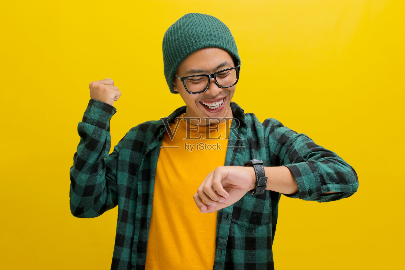 兴奋的亚洲男子戴着无边帽看手表庆祝成功照片摄影图片