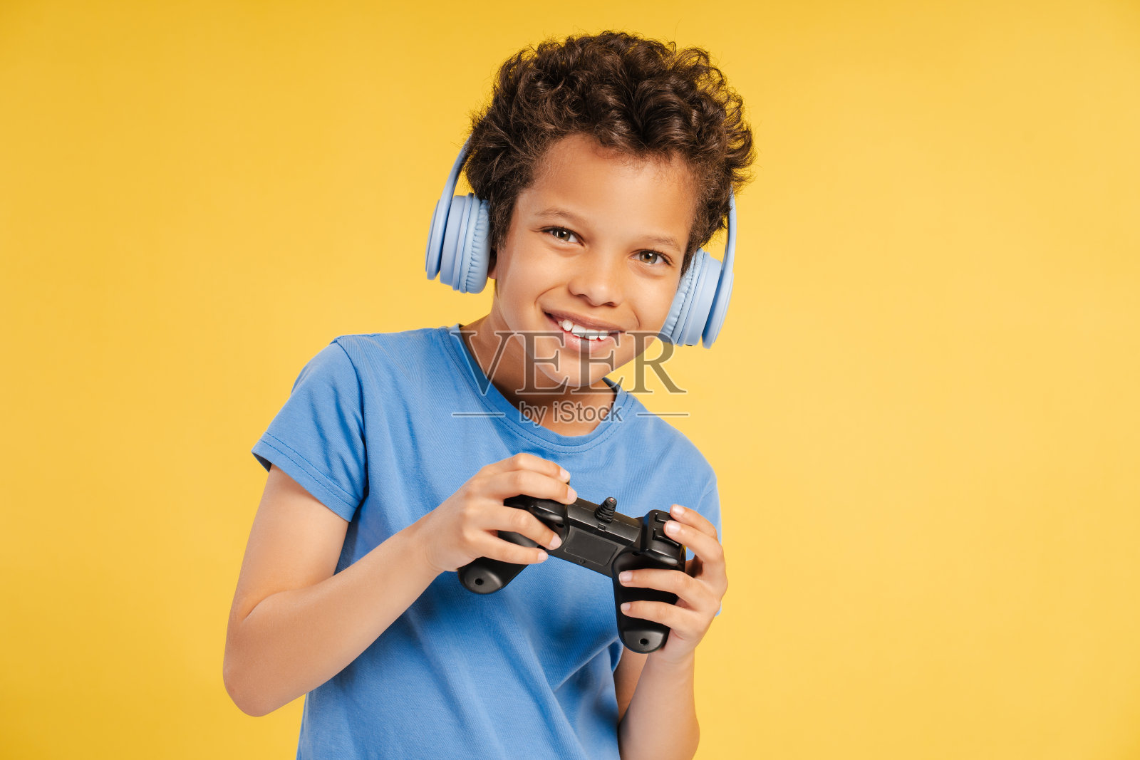 可爱的小男孩听着音乐，拿着游戏机，看着黄色背景上孤立的相机照片摄影图片