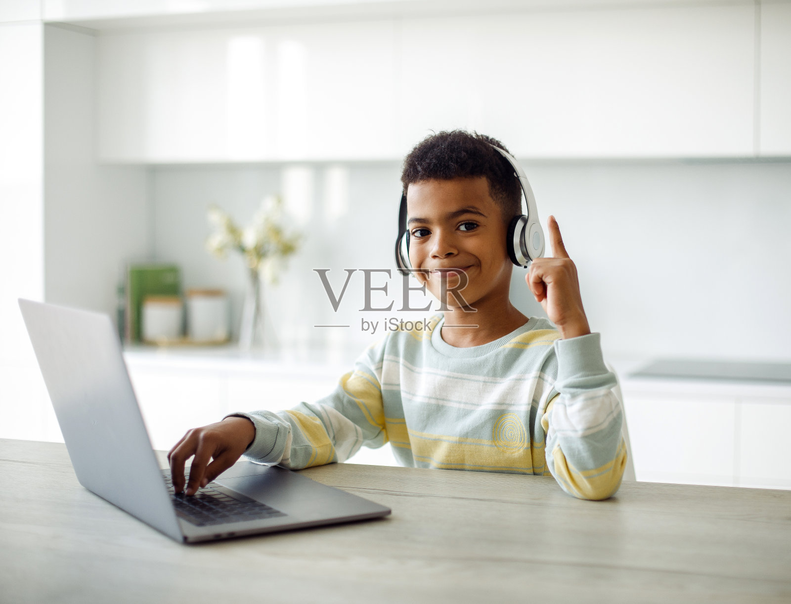 7岁的混血男孩用笔记本电脑和耳机做作业。照片摄影图片