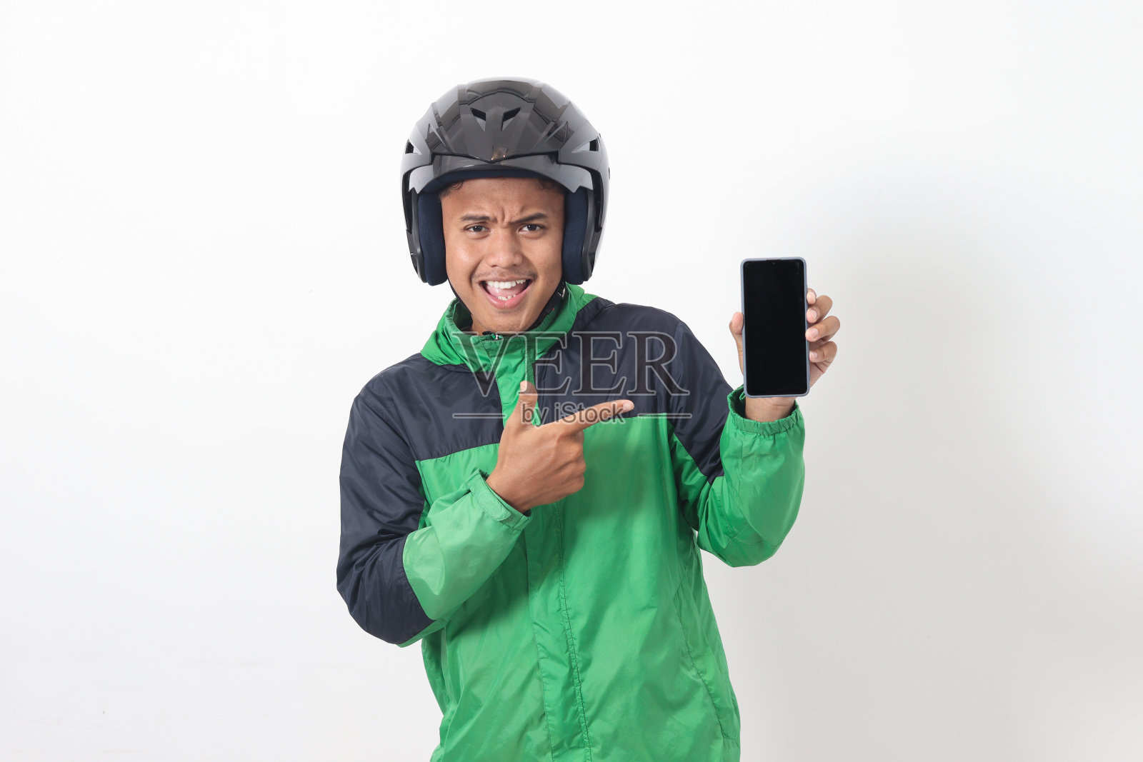 亚洲网约车司机的肖像，穿着绿夹克，戴着头盔，展示着黑屏手机。白色背景上的孤立图像照片摄影图片