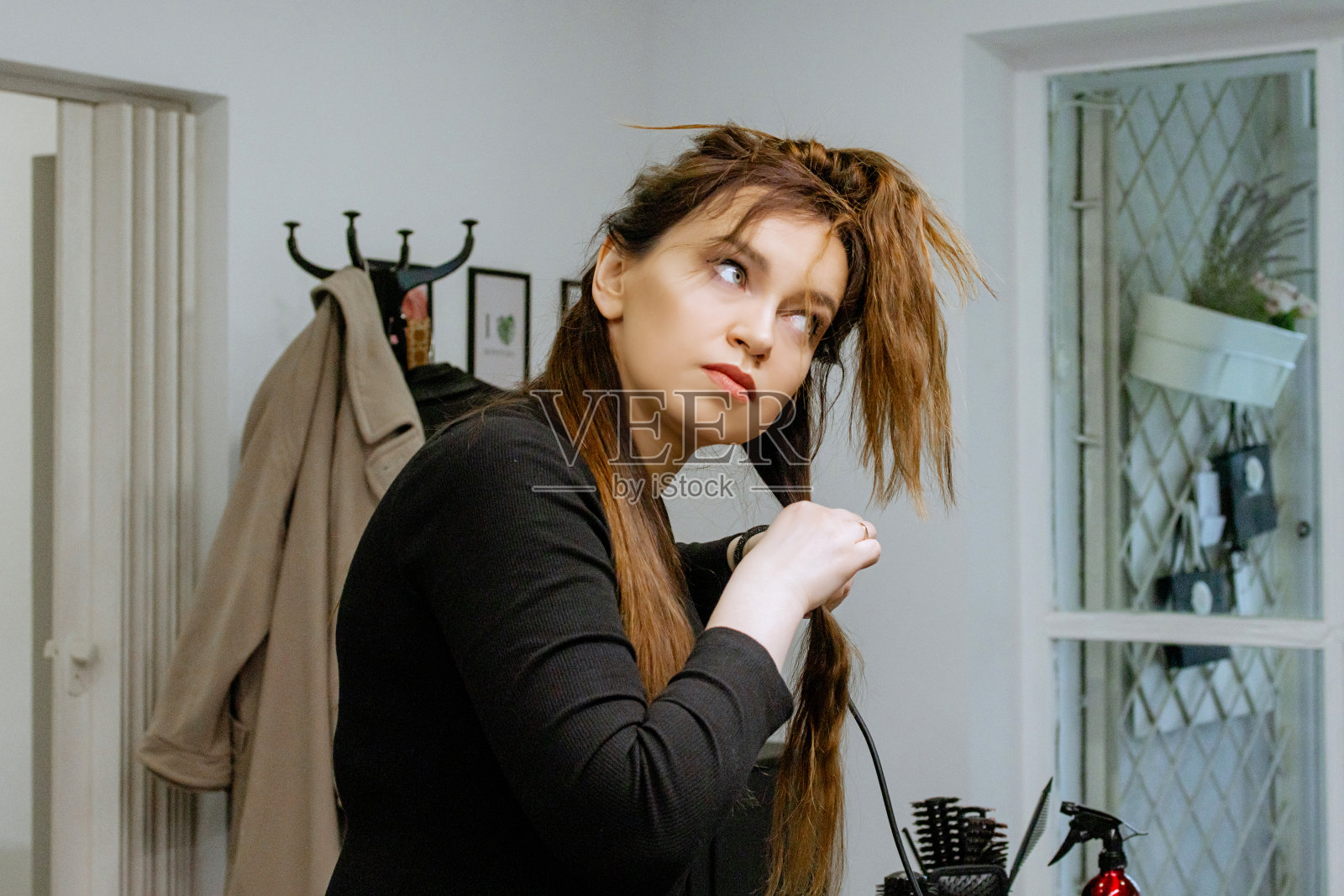 发型师在美容院用直发棒拉直自己的头发，做发型照片摄影图片